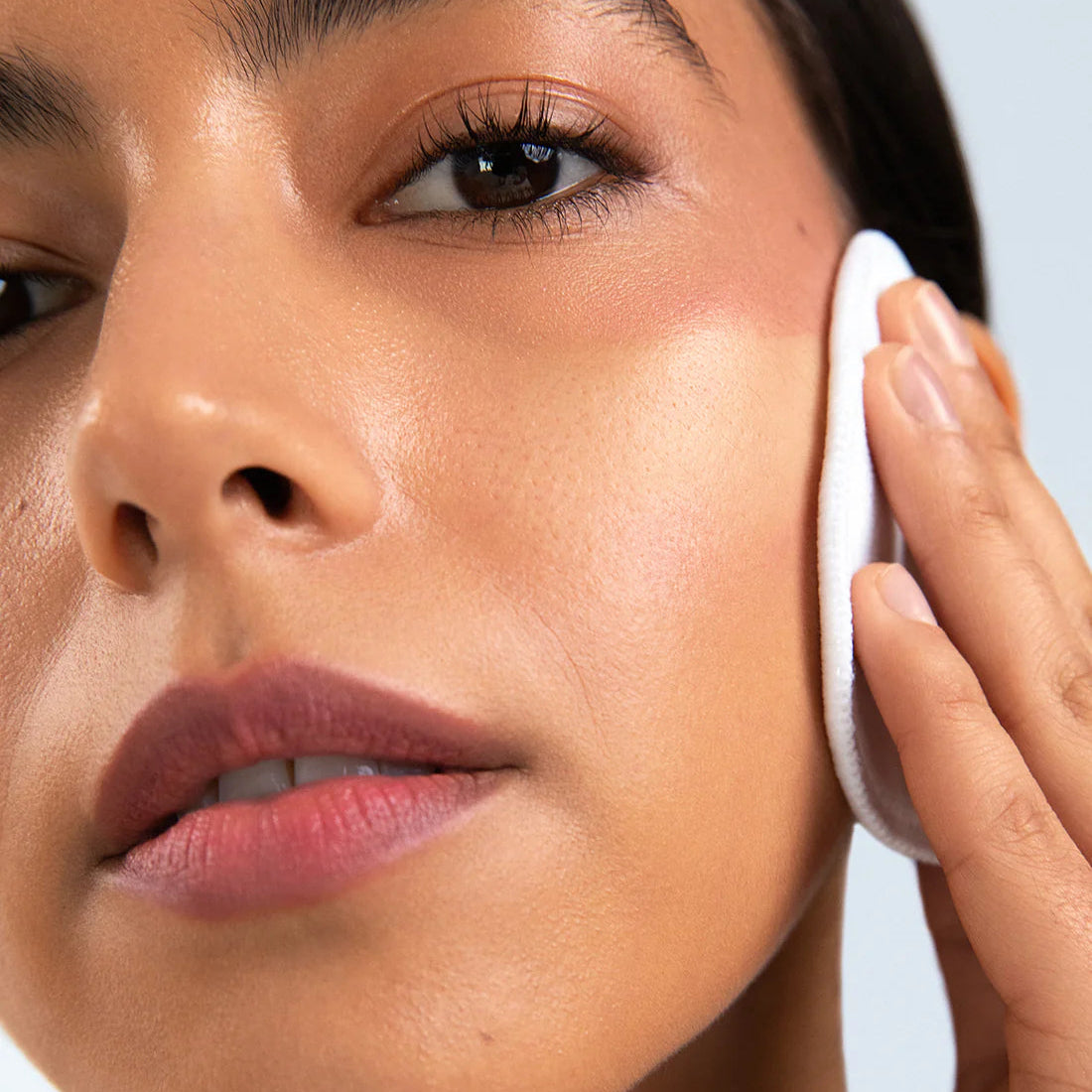 Close-up of a woman applying a white skincare product to her face against a light blue background