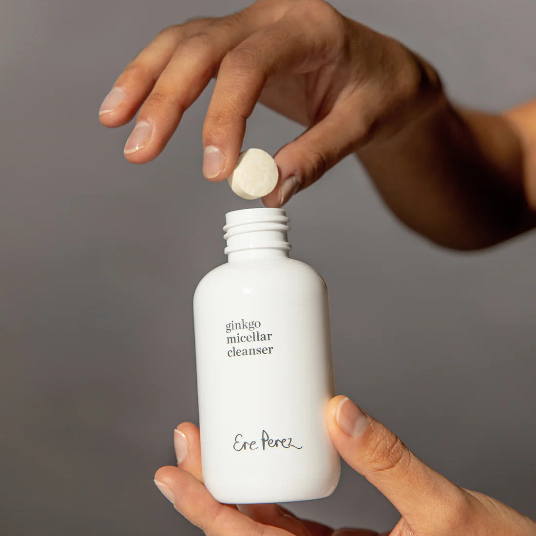 Person holding a white bottle labeled 'ginkgo micellar cleanser' by 'Eric Renee' with a gray background.