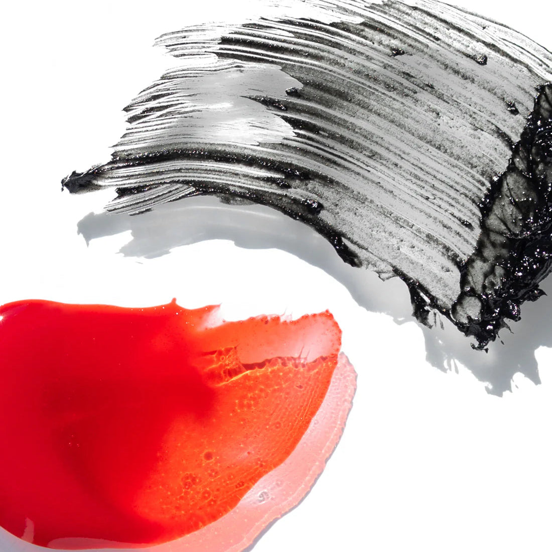 Red lip swatch next to a black and white mascara brush stroke on a white background