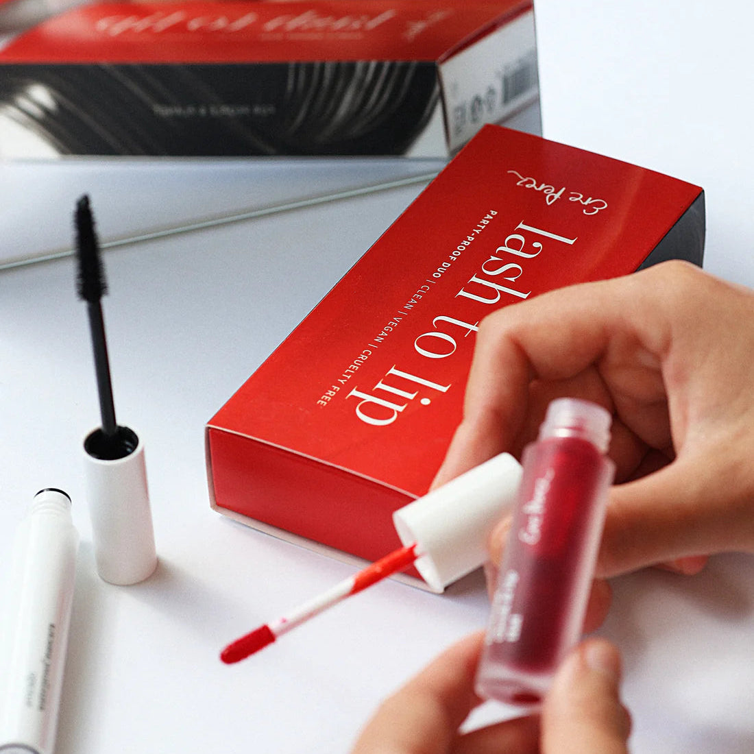 Red lip product with applicator and 'Lash to Lip' box on a white surface